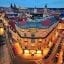 View of Prague city at night from a rooftop on a street corner, showing a road with cars below and a view of the city in the background.