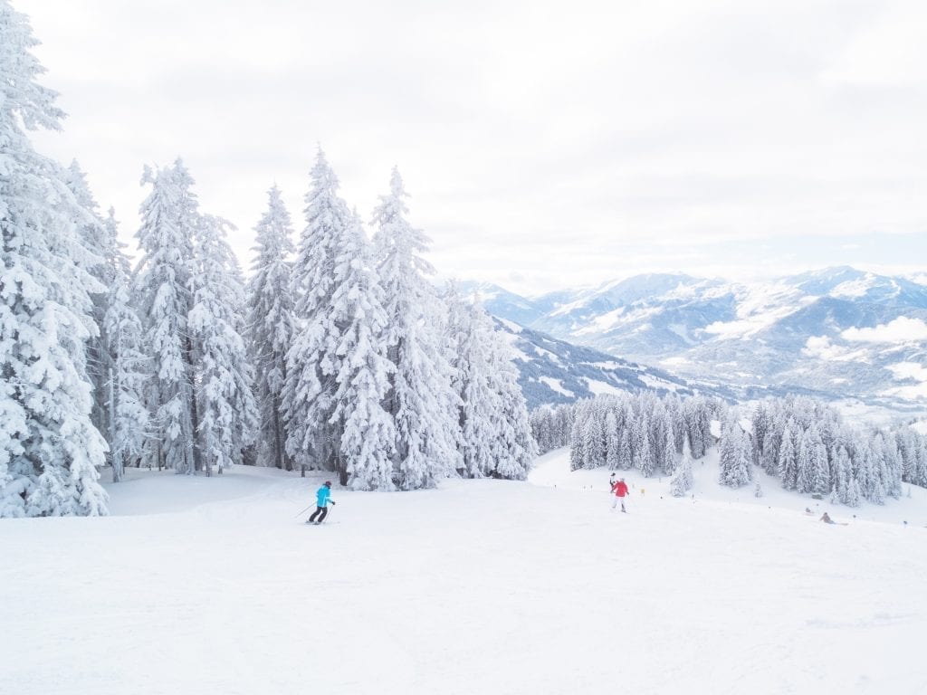 A ski slope covered in snow with people skiing and tall pine trees