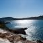 Panoramic view of the sparkling Mediterranean Sea along the rocky shoreline of Santa Ponsa, Mallorca, with sun reflecting off the water, terraced resort balconies in the foreground, and distant hills framing the bay under a clear afternoon sky—an inviting scene for travelers making the scenic journey from Palma Airport to Santa Ponsa.
