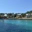 A view of a bay in Cala d'Or, with blue waters in front and a stretch of land with homes amongst vegetation behind.