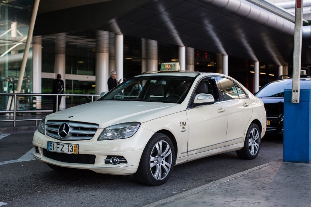 A cream airport taxi in Lisbon (sedan), parked outside the airport.