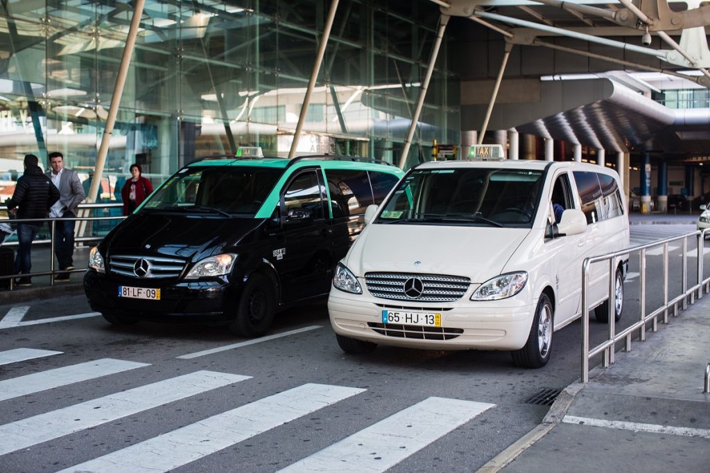 White and black minivan taxis lined up outside the airport exits. Taking a taxi from Lisbon Airport to Sintra is one of the fastest and most convinient ways to travel.