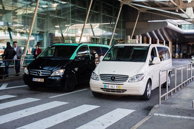 White and black minivan taxis lined up outside the airport exits. Taking a taxi from Lisbon Airport to Sintra is one of the fastest and most convinient ways to travel.