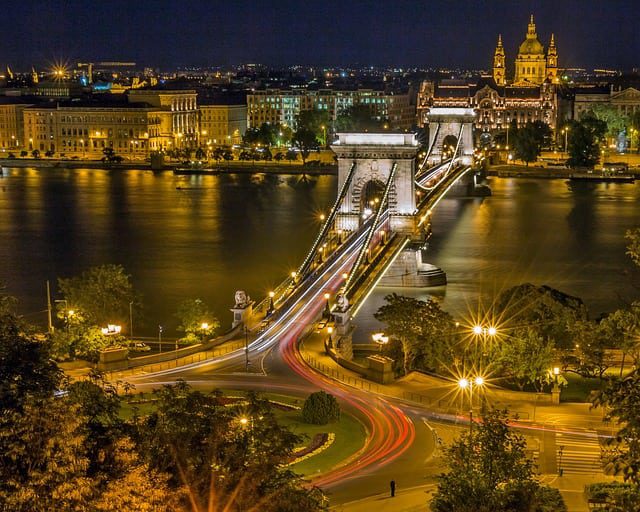 Budapest city lit up at night with a bridge crossing over a river and a large church in the background.