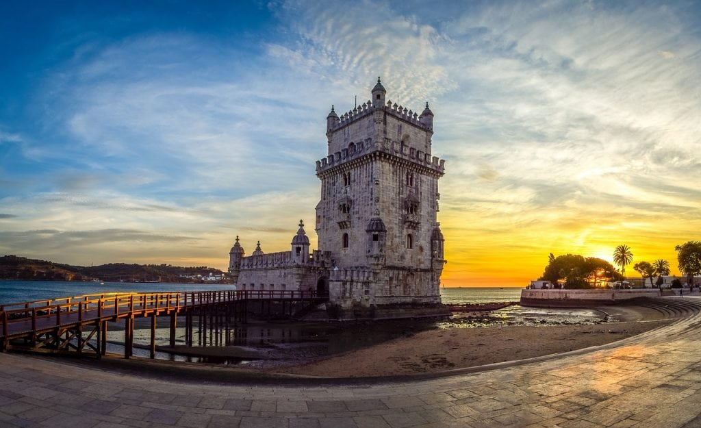 View of the Belem Tower in Lisbon, with blue water in the background and cloudy sunset skies above.