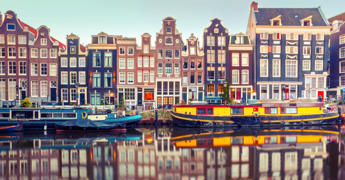 A row of narrow colorful houses with lots of windows along a waterfront with a blue and yellow boat featured in front