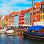 A row of colourful houses along a waterfront area, with boats parked in front.