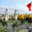 View of the Main Square of Lima with a Peruvian flag flying on the right, palm trees lining the square and colonial buldings.