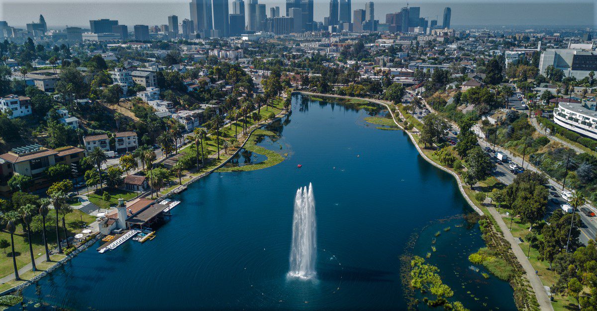 A boat leaving a trail as it travels up a lake surrounded by greenery and city buildings