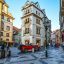 A city street in Prague lined with heritage buildings with an old-fashioned red motorcar driving along the road.