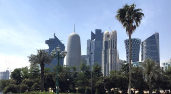 A view of Doha city with a green park and palms in front and skyscrapers behind.