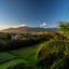 A view of San Jose with rolling green fields in front and mountains behind, with blue skies above.