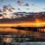 a pier disappearing into the sea with an orange sunset in the backgroun