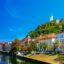 white and brown concrete buildings with red brick roofs near body of water surrounded by green trees