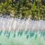 aerial photograph of white sandy beach and clear light blue green waters near green palm trees