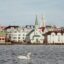 a swan swims in front of Keflavik buildings
