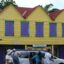 brightly painted wooden house with red roof, yellow front and purple windows framed by green lines