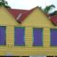 brightly painted wooden house with red roof, yellow front and purple windows framed by green lines