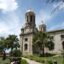 classic concrete religious building under a sunny but cloudy sky, surrounded by palm trees and green bushes in St. John's Cathedral, St. John's, Antigua and Barbuda