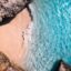 aerial view of milky blue waters near brown rock formation and a white sand beach in Aruba, Aruba