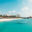 beach in Aruba, blue sky in daytime and clear blue waters with white sandy beach and town buildings in the background