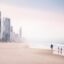people walking on the beach in daytime with the city apprearing in the background just off the shore