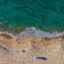 aerial view of blue-green waters and a sandy beach with people appearing in distance