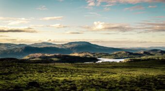 landscape view of nature, green field with mountain peaks in distance on a cloudy day