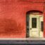 old off white wooden door with glass at against a painted red brick wall in the New Orleans French Quarter