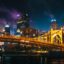 lighted bridge over body of water during night time with city lights and buildings appearing in the background
