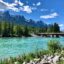 mountain peaks at distance reflecting on turquoise body of water near dark green fir trees and concrete bridge