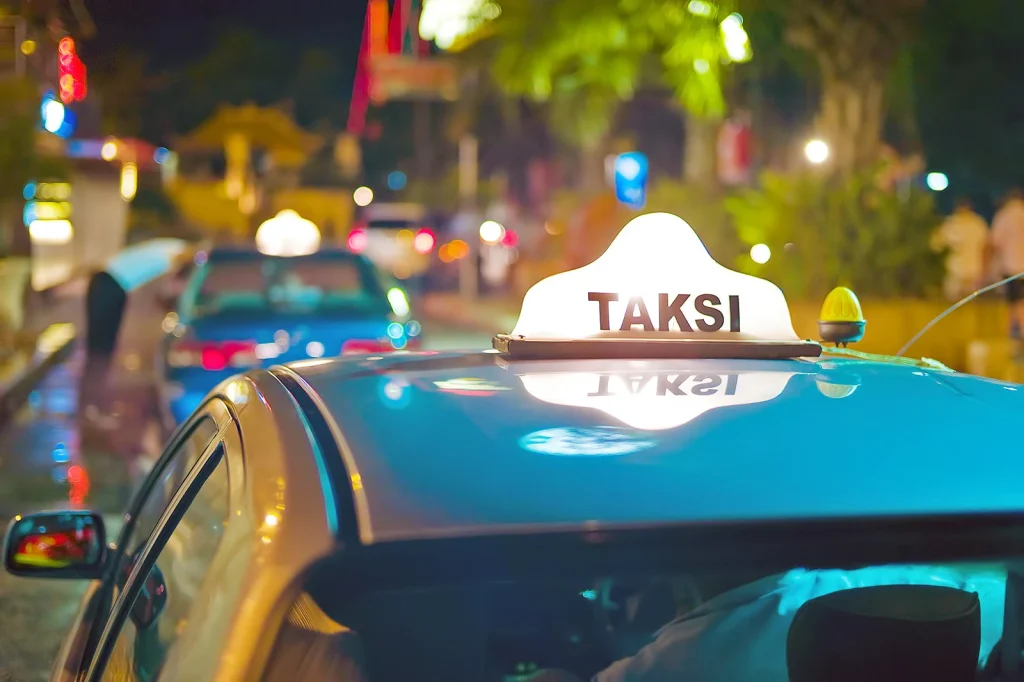 A blue Bali taxi with lighted Taksi signage on the roof.