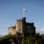 castle photographed in daytime with people entering through the doors and the Welsh flag waving in the wind