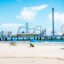 sandy beach with yellow sun-loungers. pier with amusement park in the background. Rides including rollercoasters and ferris wheels