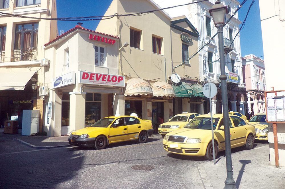 yellow cabs parked in the street with pale yellow houses in the background