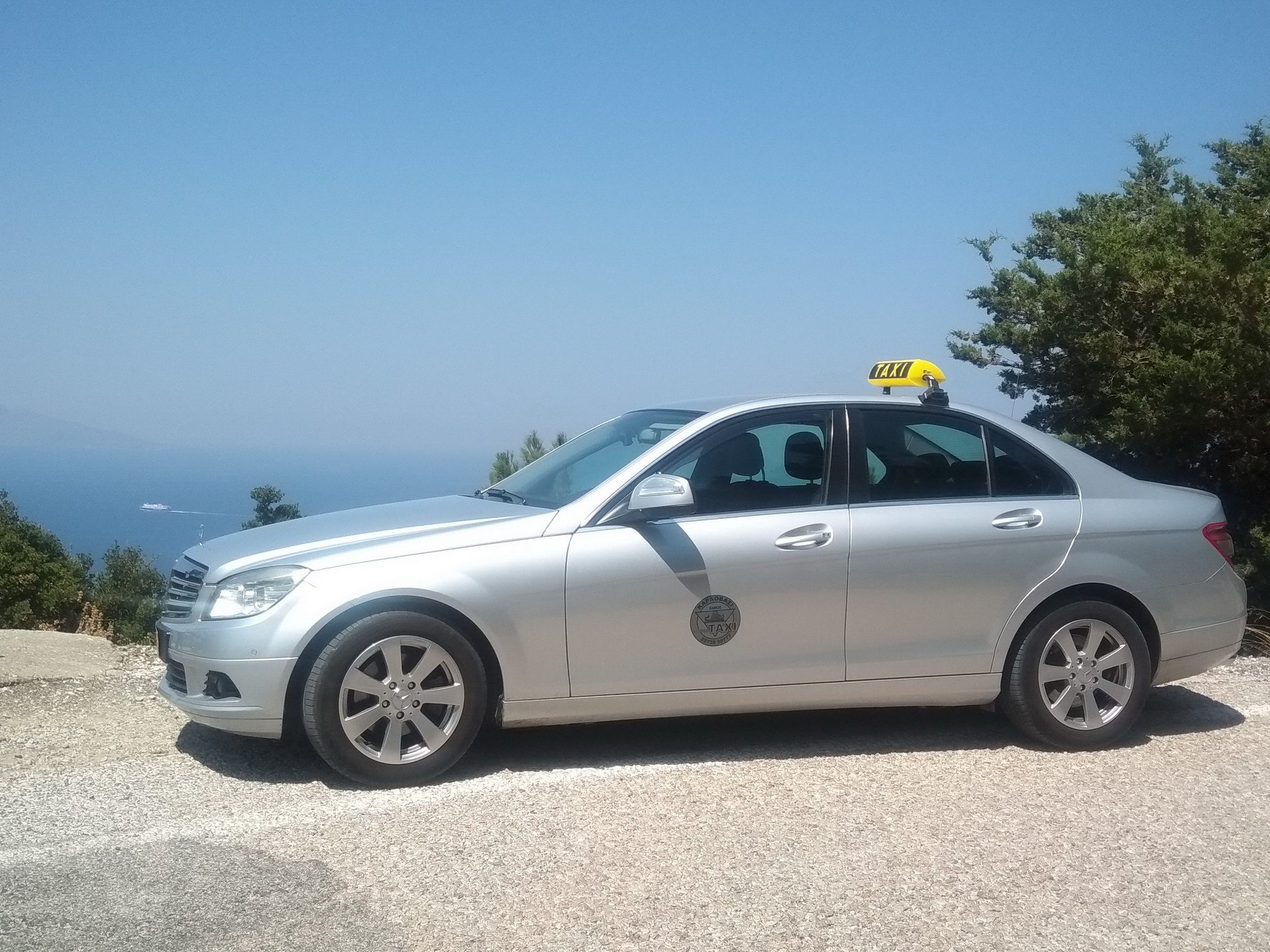 silver taxi with a signature yellow and black roof sign by a tree