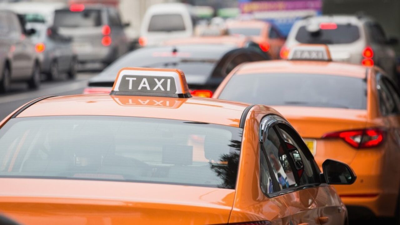 orange taxis with signature sign on roof driving in a busy street