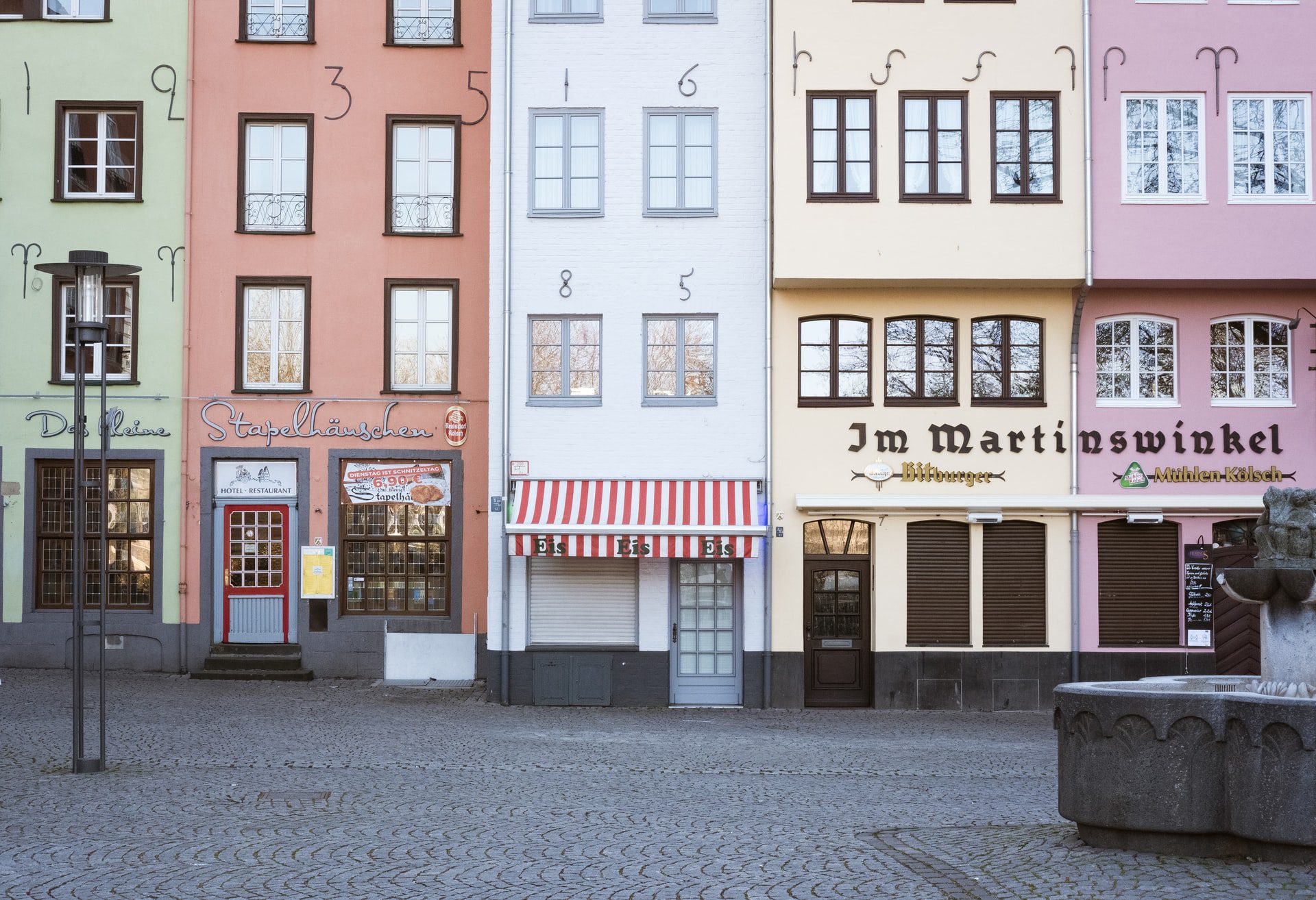 colorful shops with many small windows with numbers on them on a quiet square next to a fountain