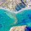 An aerial view of clear blue waters near a rocky formation and houses.