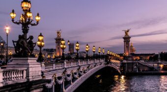 Parisian bridge with lights over a body of water at dusk.