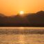 silhouettes of mountains by the sea as the sun sets behind them