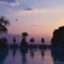 Silhouettes of palm trees, pool umbrellas, and deck chairs by swimming pool under a purple and pink sky during sunset in Tirana, Albania