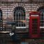 Signature red street phone booth in London with someone walking past it holding an umbrealla on a rainy day