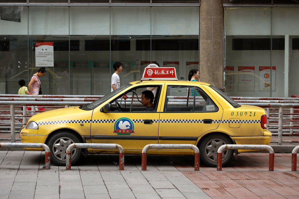 Chongqing taxi yellow taxi with checker stripe painted across it and a red sign on the roof