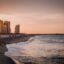sun setting behind high rise city buildings near the sea where people are hanging out in Fortaleza - CE, Brasil