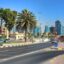 road view in Sharjah with blue high rise buildings in the background, street signs and palm trees