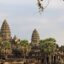 peaks of tiered buildings sprout above palm trees under a cloud covered sky