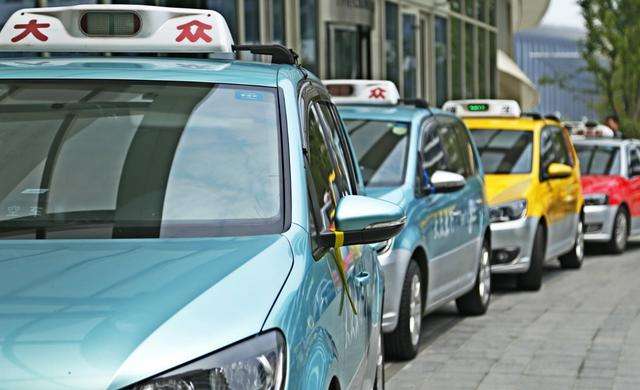 different coloured taxis lining up on the side of the road waiting for their next ride