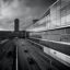 black and white photo of a large glass building and road traffic beside it under a cloudy sky