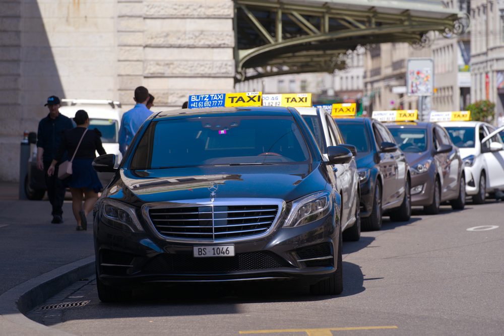 Basel taxi a mix of black and white sedan vehicles lined up at a taxi rank with a signature yellow taxi sign on their roof